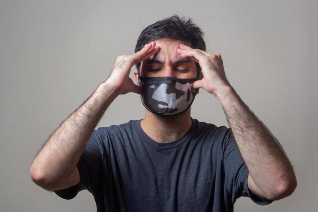 Man in a face mask with hands on head